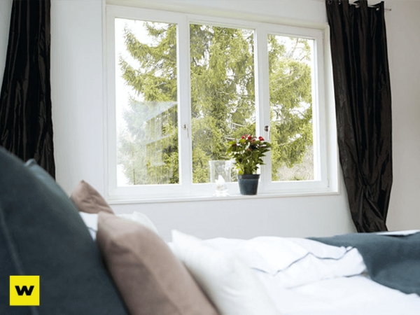 Helles Schlafzimmer mit großem Fenster, Blick ins Grüne und Pflanze auf der Fensterbank.