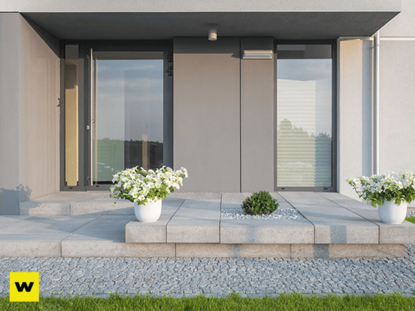 Moderner Hauseingang mit großen Fenstern, grauen Fliesen und dekorativen Blumentöpfen.