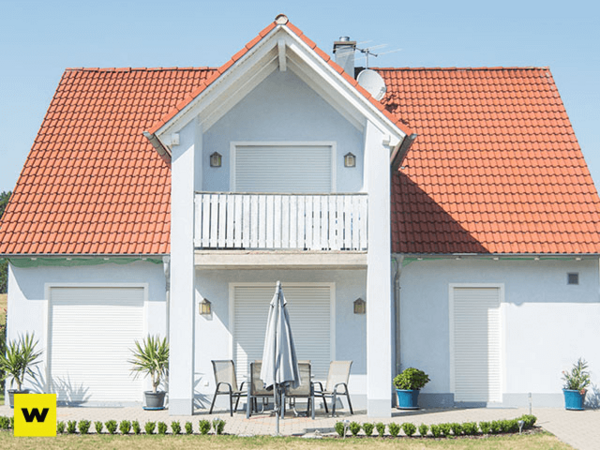 Modernes Einfamilienhaus mit rotem Satteldach, Balkon und geschlossener Terrasse.
